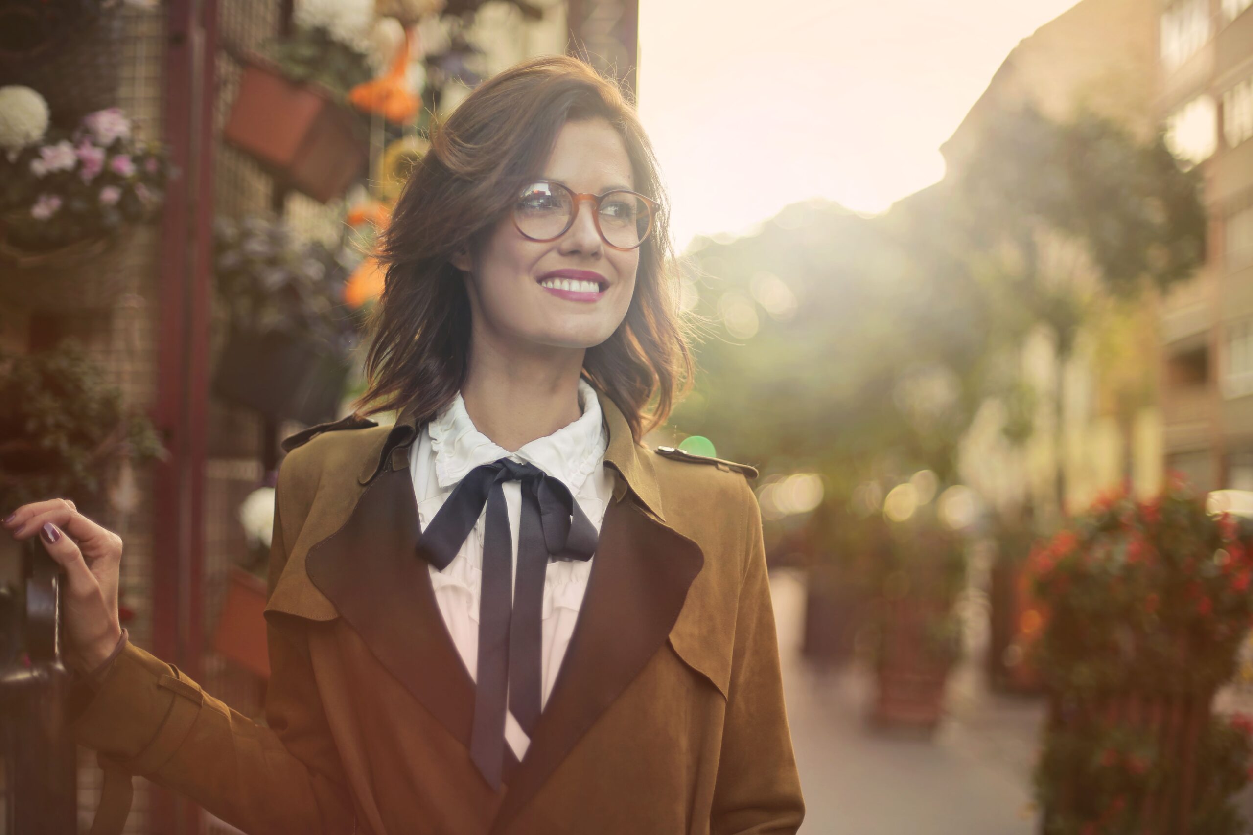 Portrait of a smiling woman in glasses and coat outdoors on a sunny day.